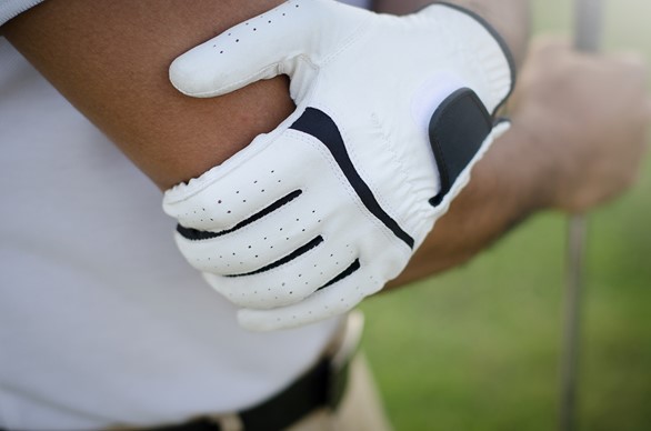 A golfer in white gloves holds his elbow, which he has injured in play.