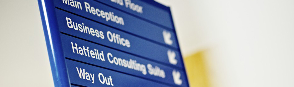 A close up of a blue informational sign in a hospital, directing to areas of the building.