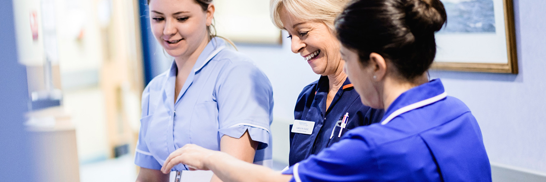 Three nurses looking down and laughing while they talk.