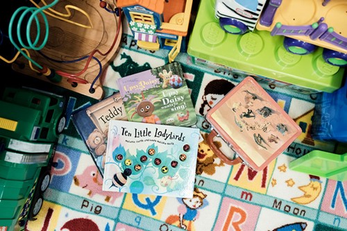 A range of childrens' books and toys on a colourful floor.